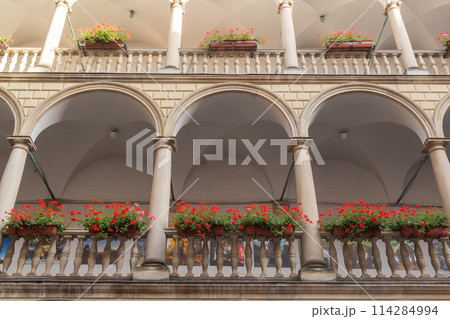 【ウクライナ】リヴィウ旧市街にあるイタリア風中庭の各階の石造のアーチと赤い花が咲くプランター 114284994