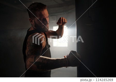 Muscular man hitting punching bag Muscular man hitting punching bag 114285269