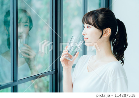 朝、窓際で水を飲む女性。 114287319