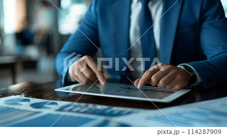 A man in a suit is using a tablet to look at a graph 114287909