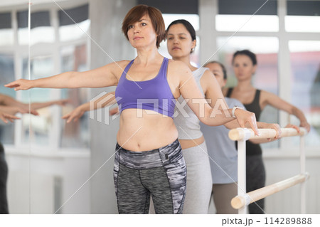 Women of different ages exercise near the ballet barre at group training session in batman batyu position 114289888