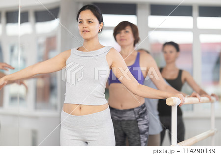 Group of women stand in second position at barre 114290139