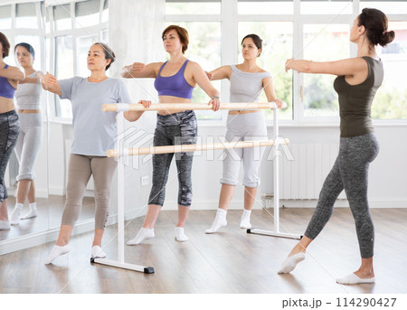 Elderly woman practicing battement tendu in beginners ballet class 114290427