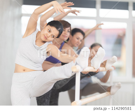 Woman with group of female fitness enthusiasts stretching at barre Woman with group of female fitness enthusiasts stretching at barre 114290581