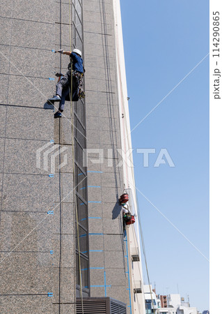 ロープにぶら下がりビルの外壁の補修をする作業員 114290865