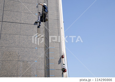 ロープにぶら下がりビルの外壁の補修をする作業員 114290866