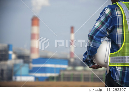 Backside Electrician engineer man hand holding White hardhat at Power stations manufacturing electrical plant. Technician worker blue hardhat helmet Engineer with steam smokestack industry background Backside Electrician engineer man hand holding White hardhat at Power stations manufacturing electrical plant. Technician worker blue hardhat helmet Engineer with steam smokestack industry background 114292307