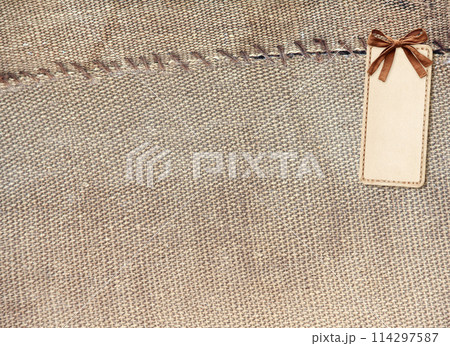 Organic eco paper price tag with bow on old burlap. Eco-friendly background with paper label from recycled carton material on rustic bag texture. Nostalgic scrapbooking style. Copy space for text 114297587
