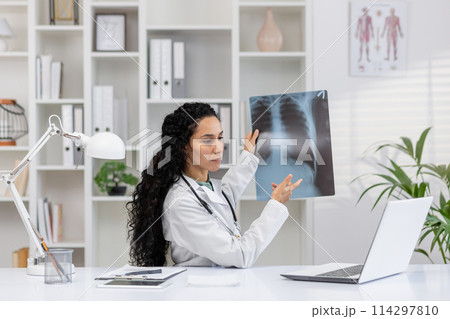 A professional female doctor examines a chest X-ray in her well-equipped medical office, indicating diagnosis and patient care. 114297810