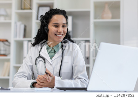 Smiling female doctor wearing a headset for an online consultation in a bright medical office. She embodies professionalism and approachability. 114297852