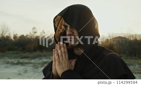 Religious Monk Wears His Hood And Prays In Nature At Sunset Religious Monk Wears His Hood And Prays In Nature At Sunset 114299584
