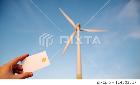 A person holds a credit card next to a wind turbine A person holds a credit card next to a wind turbine 114302517