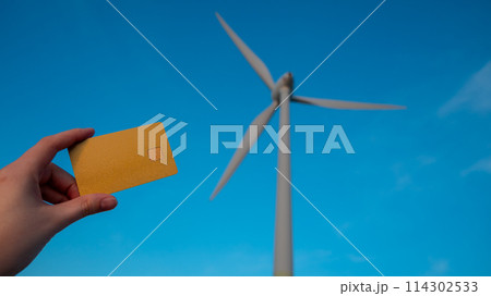 A person holding a credit card next to a wind turbine A person holding a credit card next to a wind turbine 114302533