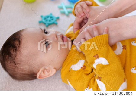 A mother dressing her little baby boy boy at home. childhood parenthood and growing up family concept real people 114302804