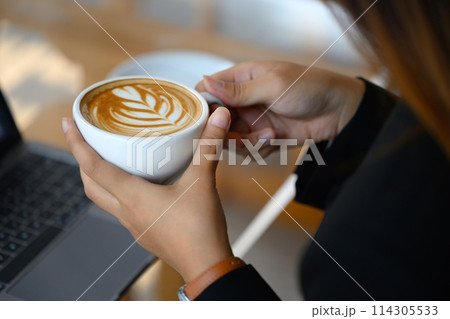 Close up shot of female hands holding cup of coffee with beautiful latte art 114305533