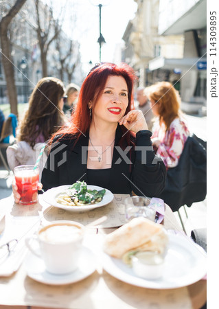 Millennial woman eating italian pasta at restaurant on the street in spring. Concept of Italian gastronomy and travel. Stylish woman with red hair Millennial woman eating italian pasta at restaurant on the street in spring. Concept of Italian gastronomy and travel. Stylish woman with red hair 114309895