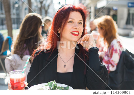 Beautiful happy millennial woman with long red hair enjoying italian pasta in a street cafe 114309902