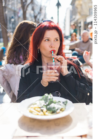 Beautiful happy woman with long red hair enjoying cocktail in a street cafe Beautiful happy woman with long red hair enjoying cocktail in a street cafe 114309965