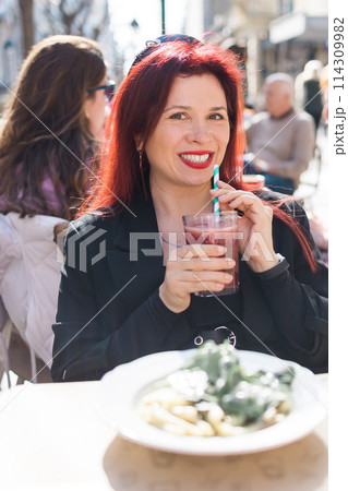 Beautiful happy woman with long red hair enjoying cocktail in a street cafe 114309982