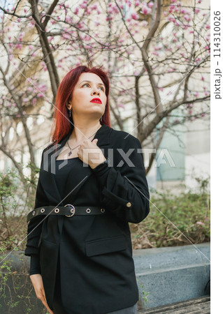 Woman with magnolia flowers surrounded by blossoming trees. Beauty and seasonal change and spring bloom season concept. 114310026