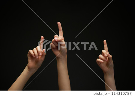 Three children's, teenager's hands pointing with index finger up against black background. Arms gesturing. Important information. Three children's, teenager's hands pointing with index finger up against black background. Arms gesturing. Important information. 114310787