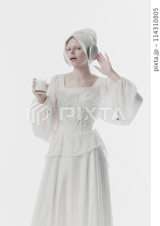 Young lady, beautiful woman wearing old fashion clothes listening music in headphones and drinks milk against white studio background. 114310805