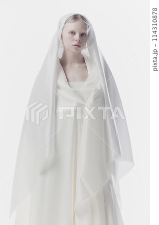 Portrait of young woman with pale skin and blonde hair looking calmly at camera, as maid or angel against white studio background. 114310878