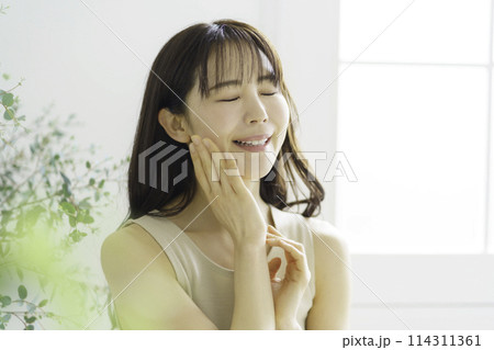 頬に手を当てて目を閉じる笑顔の若い女性のポートレート 114311361