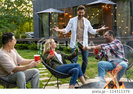 Multiethnic friends gathering together at garden near fire grill enjoying outdoor party Multiethnic friends gathering together at garden near fire grill enjoying outdoor party 114311379