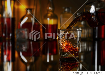 Pouring whiskey from a bottle into a glass. 114313243