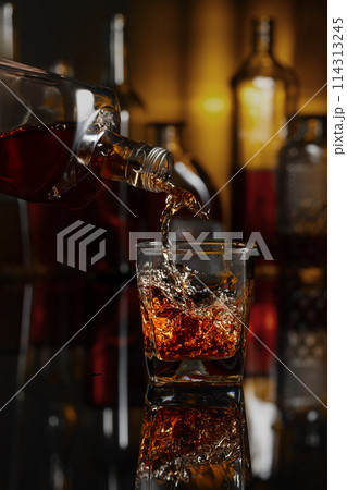 Pouring whiskey from a bottle into a glass. Pouring whiskey from a bottle into a glass. 114313245