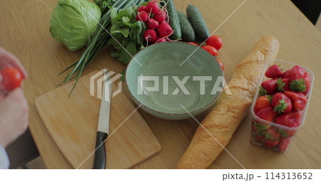 Young woman cutting cherry tomatoes on wood cutting board for fresh salad. Healthy food concept. Young woman cutting cherry tomatoes on wood cutting board for fresh salad. Healthy food concept. 114313652