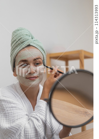 Towel-Clad Radiance: Wrapped in a towel, she meticulously applies a facial mask for anti-aging, moisture, and skin perfection. Towel-Clad Radiance: Wrapped in a towel, she meticulously applies a facial mask for anti-aging, moisture, and skin perfection. 114313993