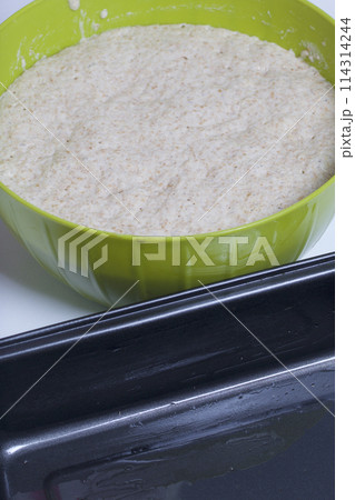 Baking bread at home. Wholemeal dough lies in a container. Near metal baking dish for bread. Baking bread at home. Wholemeal dough lies in a container. Near metal baking dish for bread. 114314244
