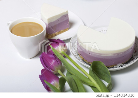 Blueberry cheesecake. A piece of ready-made dessert on a saucer. Jelly layers of different colors are visible. Near a cup of coffee and a bouquet of tulips. 114314310