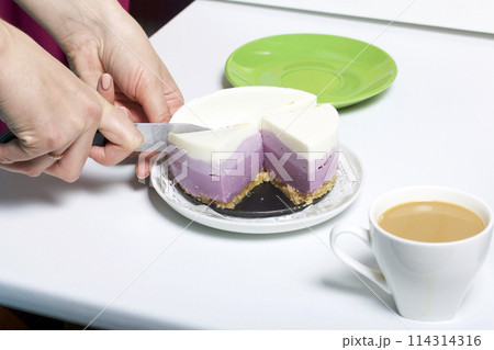 Blueberry cheesecake. A woman cuts a ready-made dessert into pieces. Jelly layers of different colors are visible. 114314316