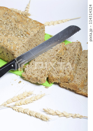Baking bread at home. A loaf of freshly baked wholegrain bread with sunflower seeds lies on a cutting board. Bread slices and a knife are visible. Baking bread at home. A loaf of freshly baked wholegrain bread with sunflower seeds lies on a cutting board. Bread slices and a knife are visible. 114314324