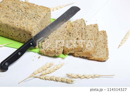 Baking bread at home. A loaf of freshly baked wholegrain bread with sunflower seeds lies on a cutting board. Bread slices and a knife are visible. Baking bread at home. A loaf of freshly baked wholegrain bread with sunflower seeds lies on a cutting board. Bread slices and a knife are visible. 114314327