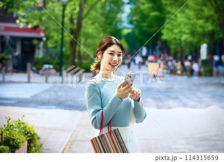 ショッピングしながらスマホを操作するオシャレな若い女性 ショッピングしながらスマホを操作するオシャレな若い女性 114315659
