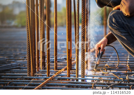 A welder welds a steel frame from reinforcement for reinforced concrete structures at a construction site. 114316520
