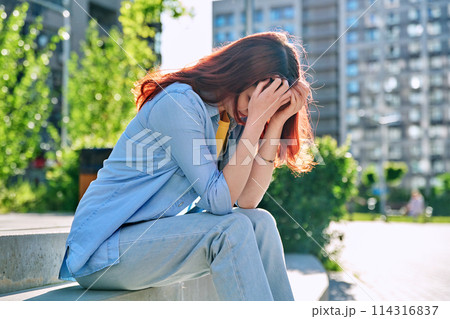 Upset sad unhappy young female sitting outdoor on steps 114316837
