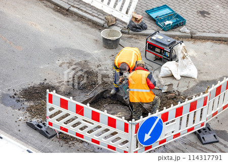 Road workers are repairing a city sewer manhole on a fenced section of the road outdoor. 114317791