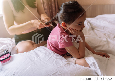 Mom braids her daughter's hair while sitting in bed Mom braids her daughter's hair while sitting in bed 114318002