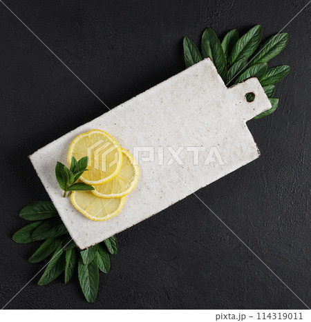 Lemon and mint leaves served on ceramic kitchen board on black rustic table, ingredient for summer cocktails and lemonade, top view Lemon and mint leaves served on ceramic kitchen board on black rustic table, ingredient for summer cocktails and lemonade, top view 114319011