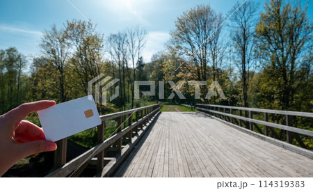 A person holding a white credit card in front of a bridge 114319383