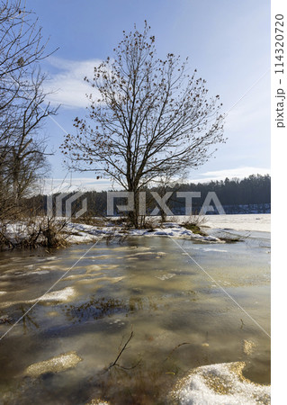 the ice-covered surface of the river in the winter season 114320720
