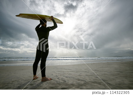 Man, surfer and wetsuit at beach for waves, sport or exercise on sandy shore in outdoor fitness. Rear view of male person or athlete with surfboard for surfing on ocean coast, sea or water in nature 114322305