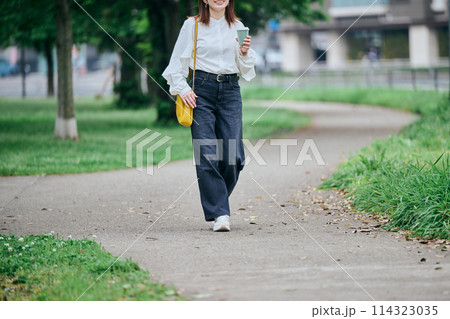 コーヒーカップを持ちながら歩く若い女性 114323035