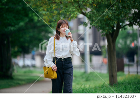 コーヒーを飲みながら歩く若い女性 114323037
