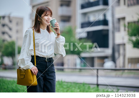 コーヒーを飲みながら歩く若い女性 114323038